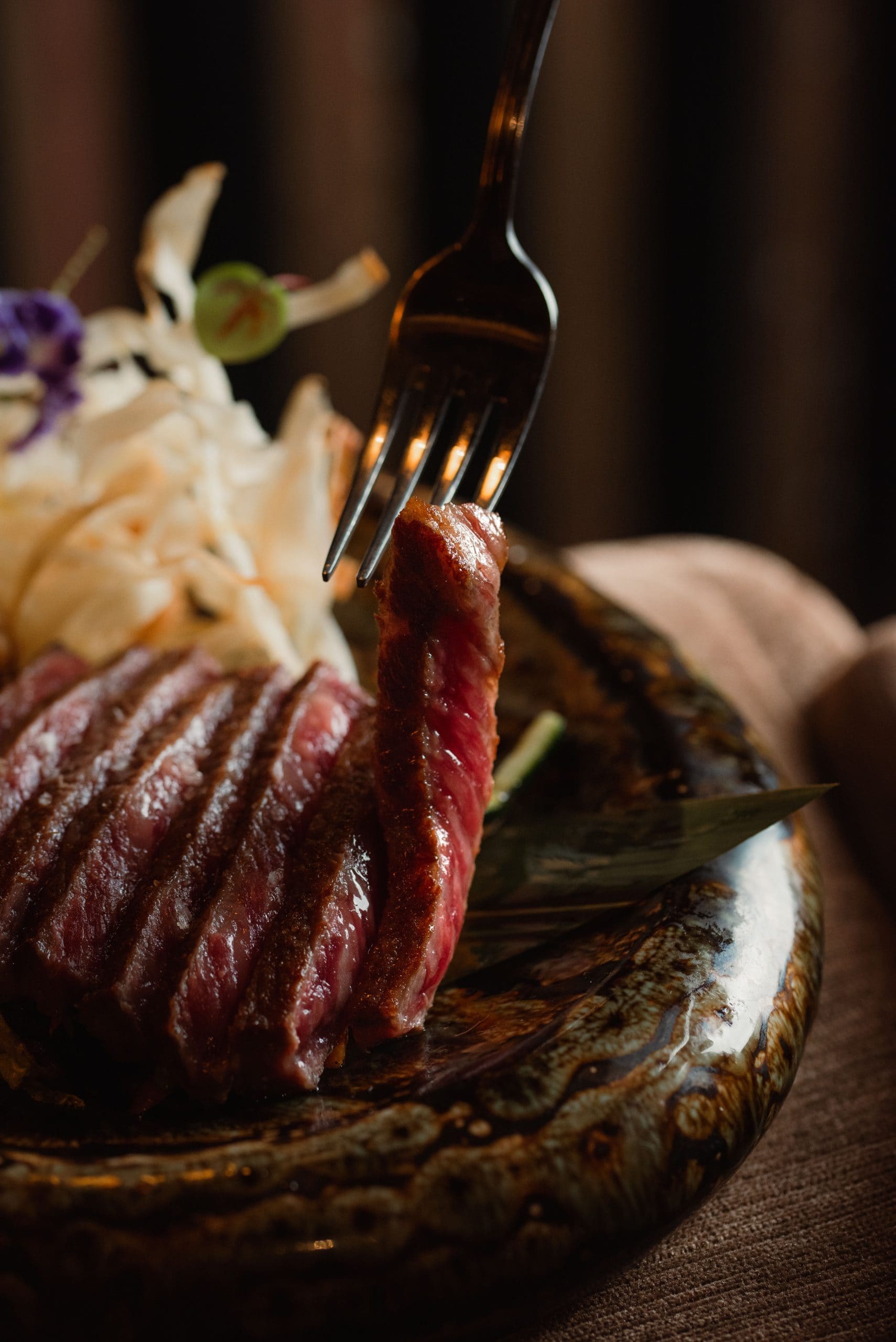 Piece of steak on a fork over a decorated plate