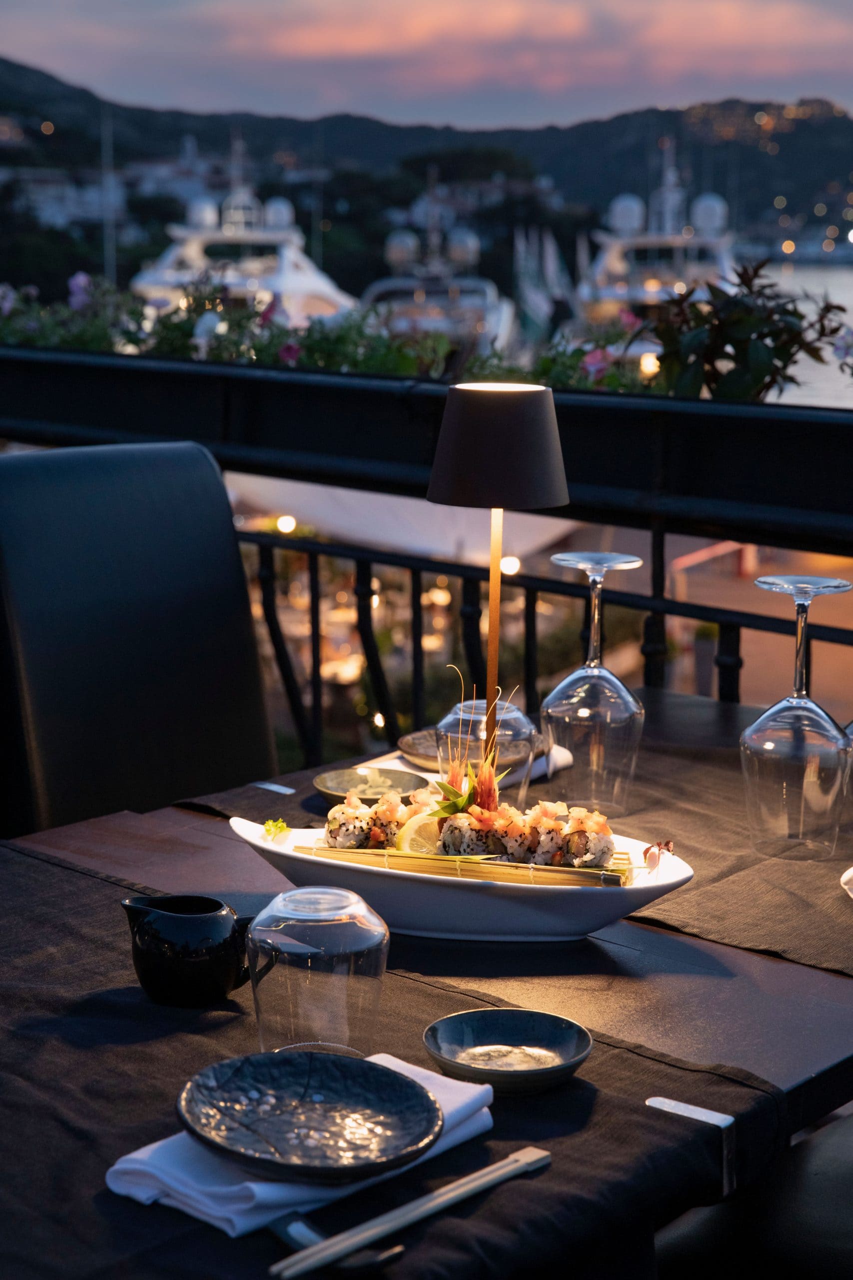 Tavolo apparecchiato con piatti di sushi al tramonto su terrazza vista mare a Porto Cervo.