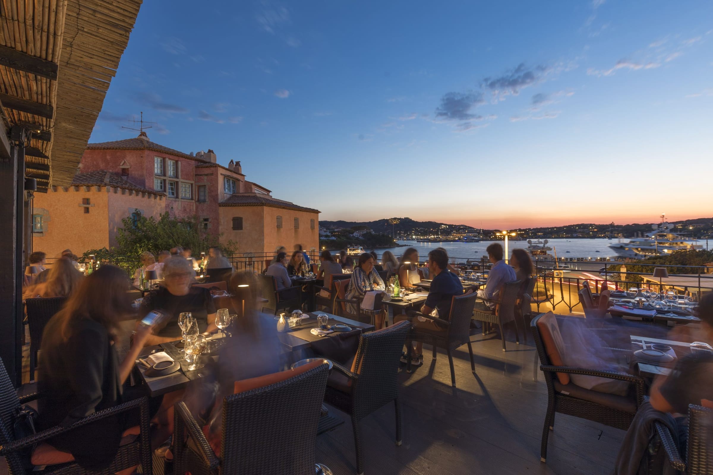 Persone cenano all'aperto con vista sul mare al tramonto