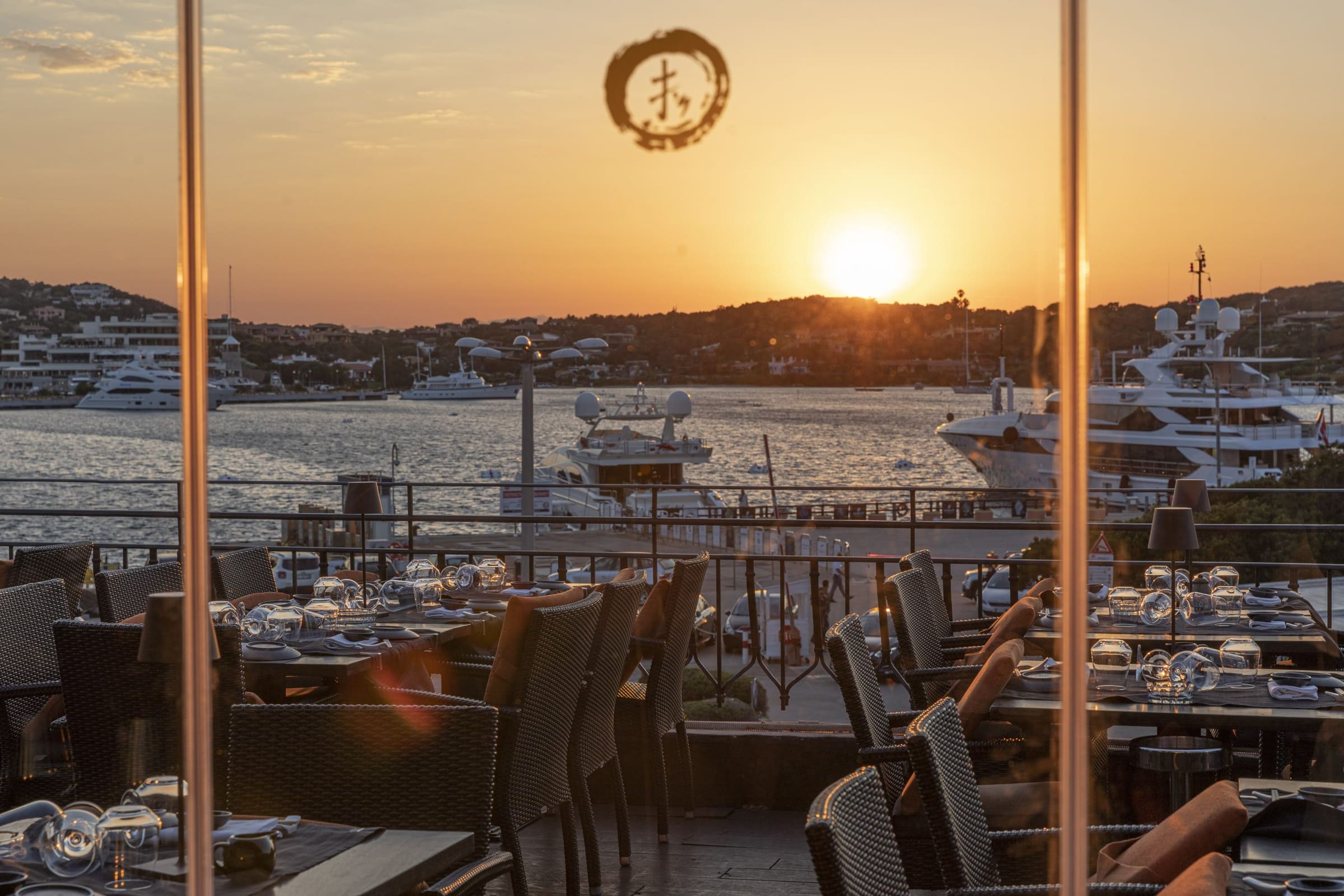 Tramonto su una marina con yacht e tavoli apparecchiati in primo piano